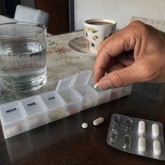 Pastillero semanal con pastillas y un vaso de agua en la mesa